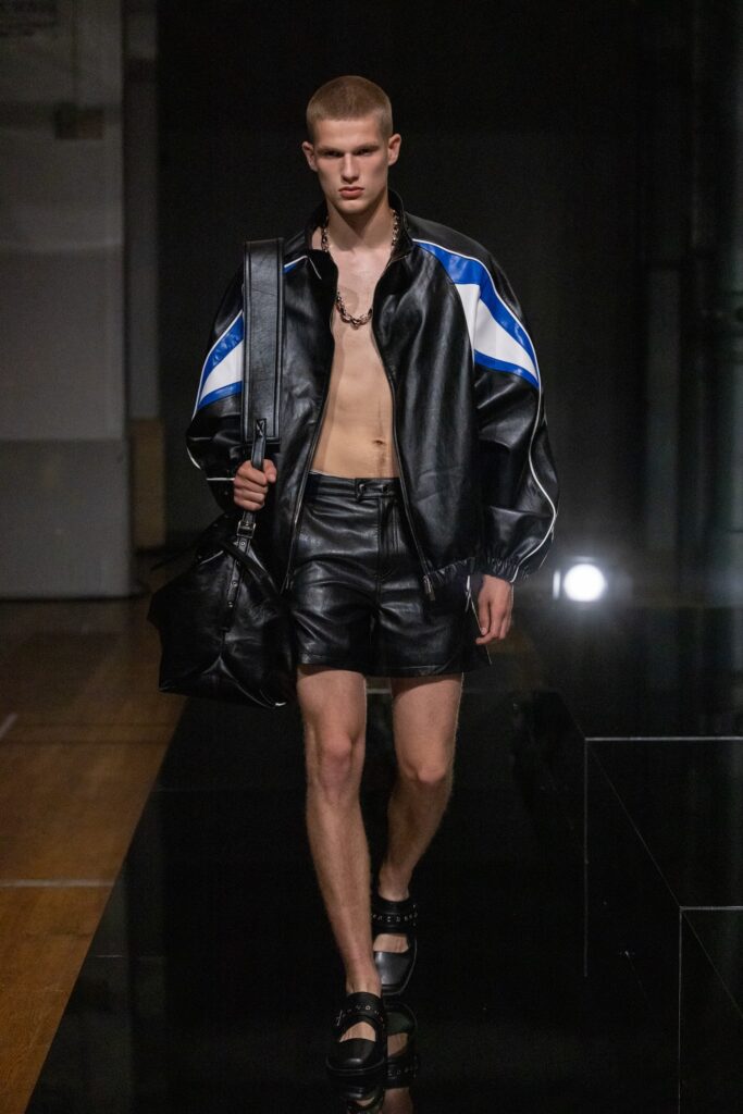 A fitted black leather jacket with short sleeves paired with matching leather shorts featuring an asymmetric design.