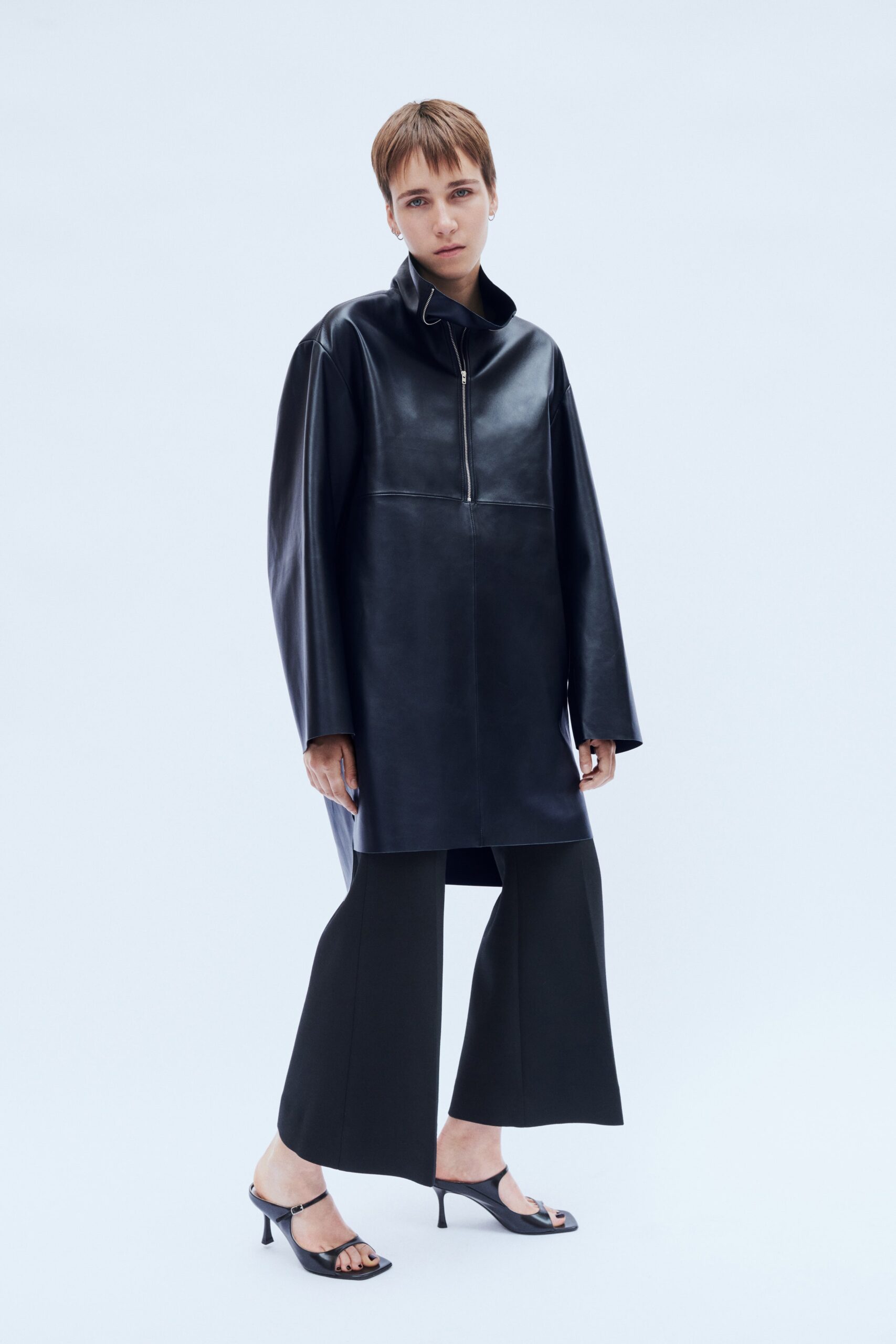 A relaxed black leather jacket with a collared neckline paired with black pants featuring an asymmetric design.