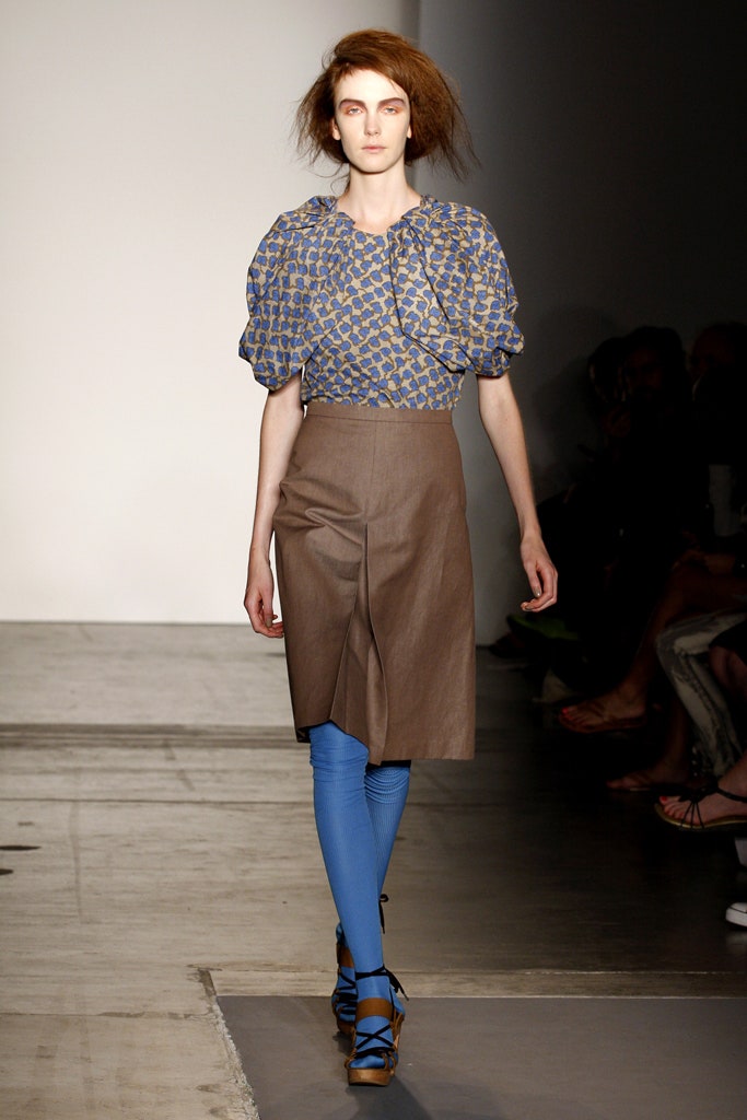A fitted blue cotton blouse with short sleeves paired with a pleated brown skirt.