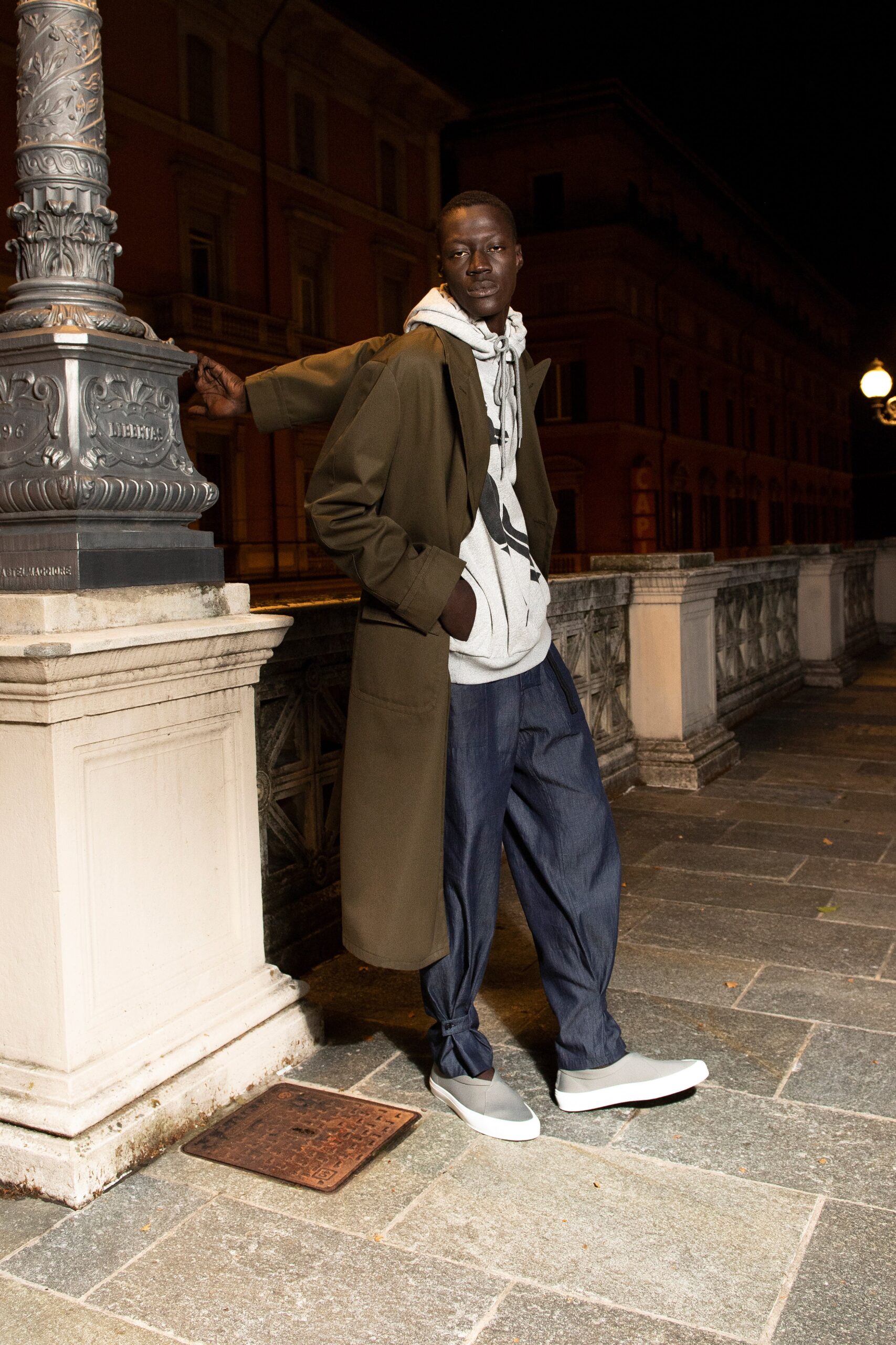 A relaxed green coat layered over a gray hooded sweatshirt with denim pants.