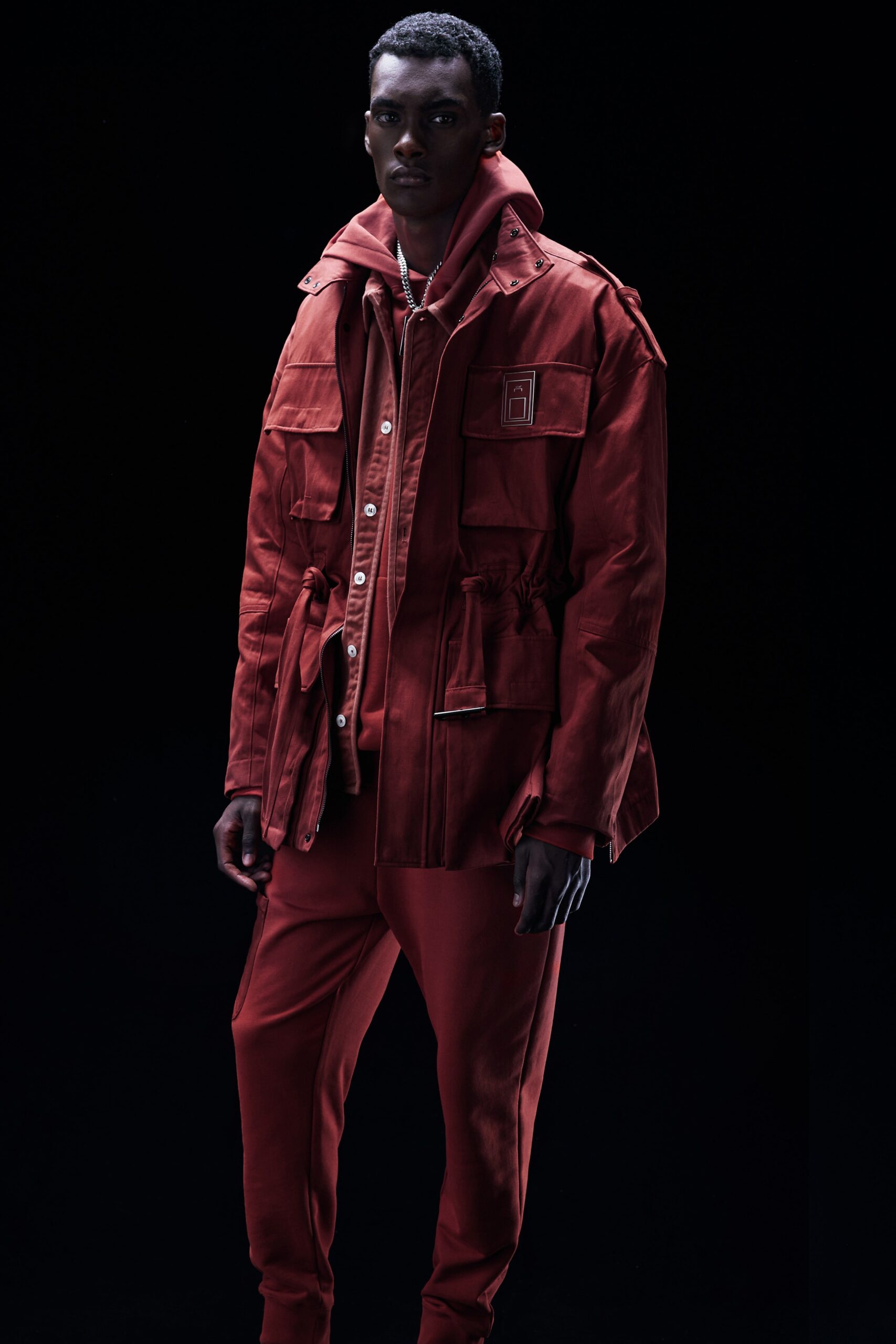 This relaxed jacket in a vibrant red is complemented by matching pants, creating a cohesive look. The long sleeves and collared design add structure, while the zippered and buttoned details enhance its utilitarian appeal.