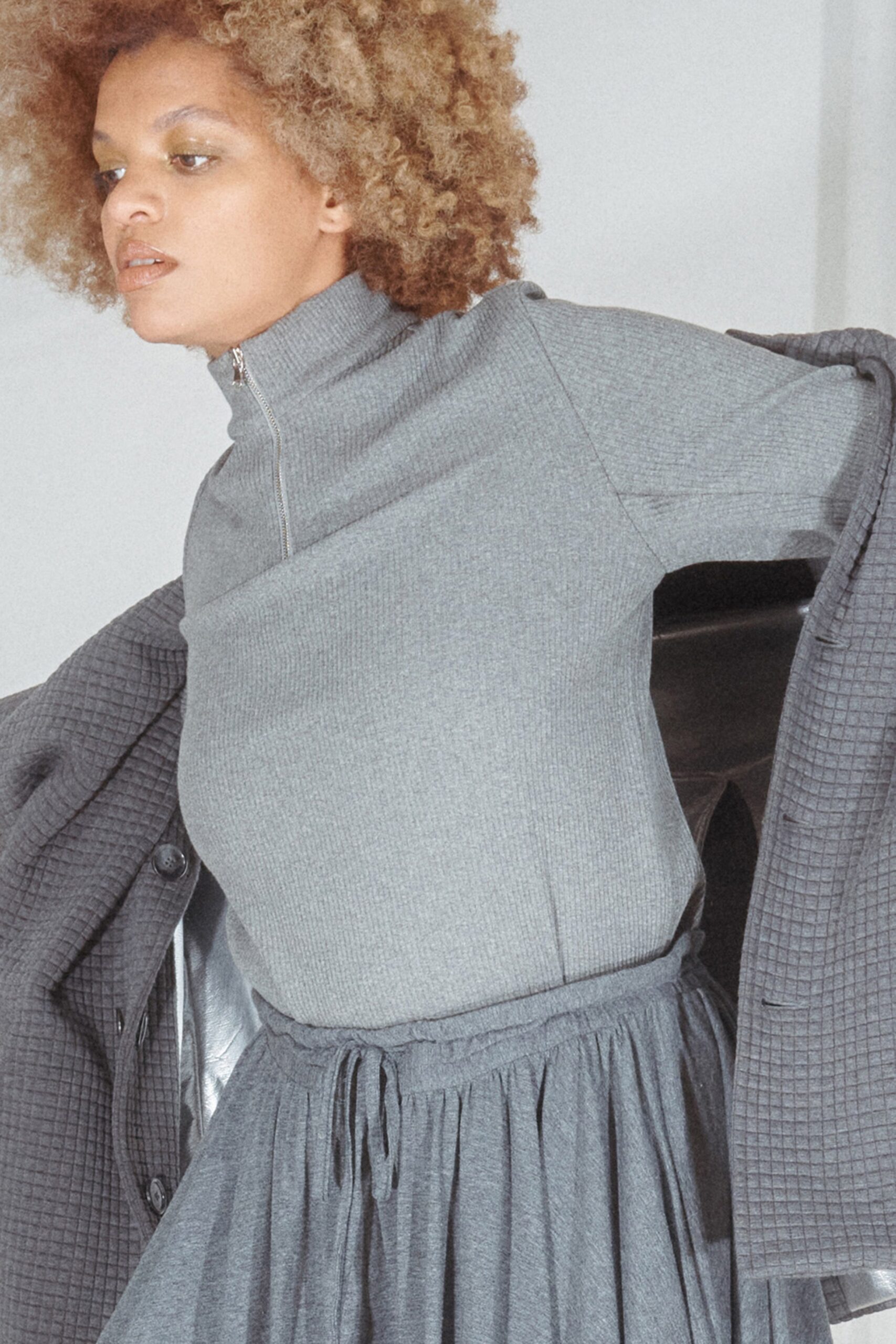 This relaxed dress features a tiered silhouette in soft gray cotton, complemented by a structured jacket. The high-neck design adds a contemporary edge, while the layering creates a dynamic visual flow.