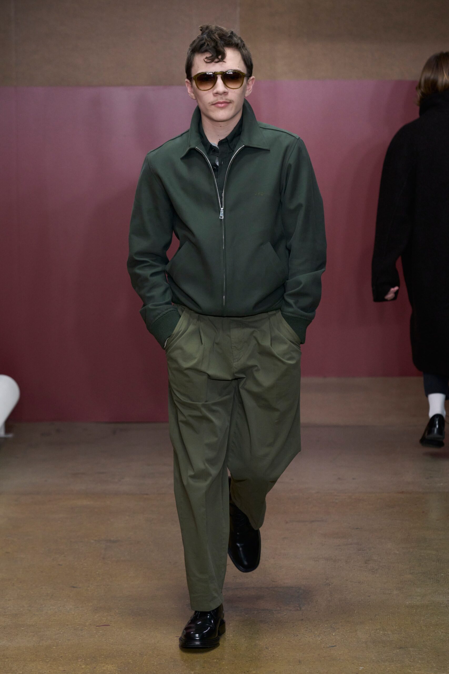 A relaxed green cotton jacket with long sleeves and collared design, paired with pleated gray pants.