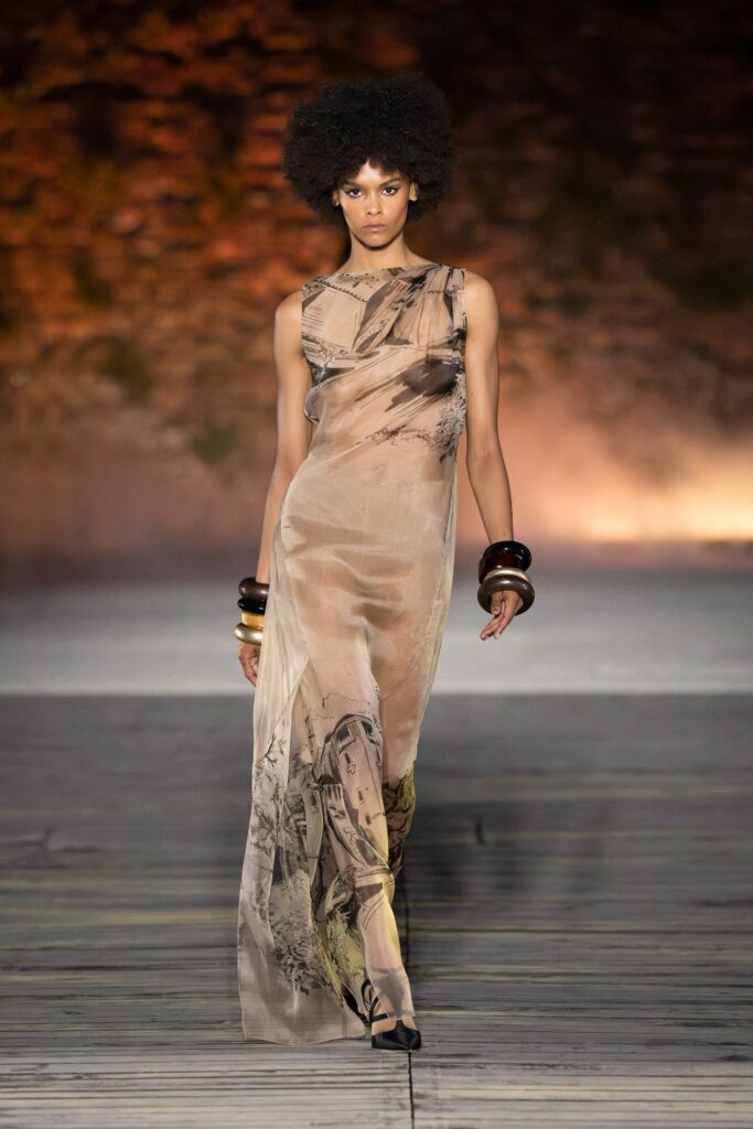 A fitted beige silk sleeveless dress with a high neckline and asymmetric design.