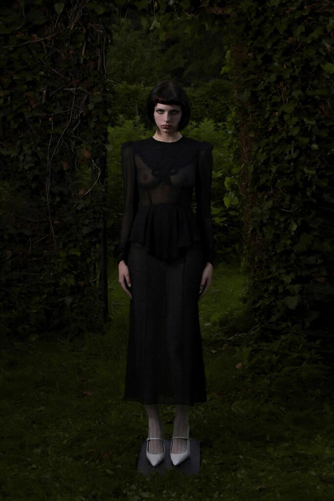 A fitted black silk dress with long sleeves and a high neckline featuring a layered design.