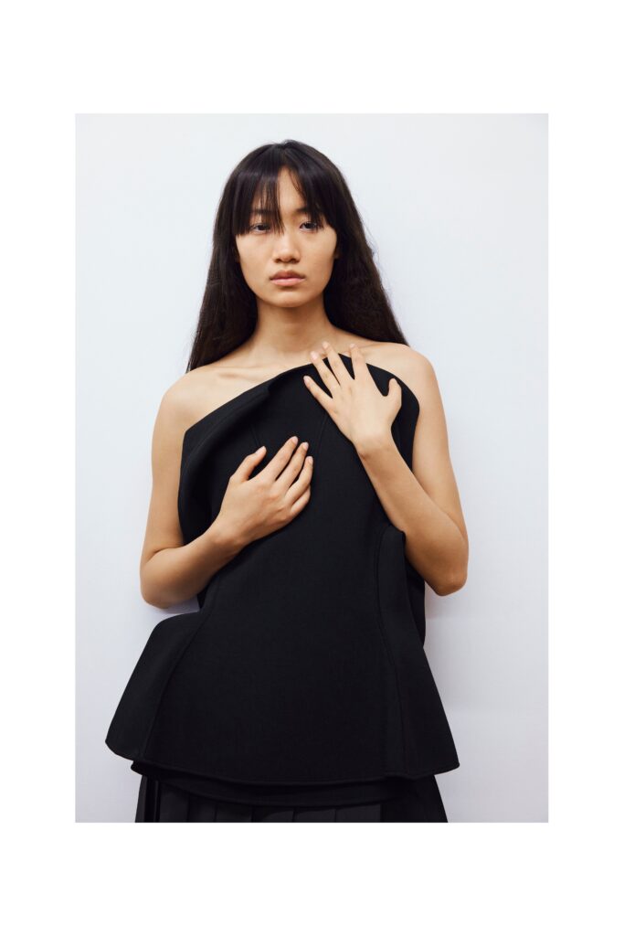 A fitted black sleeveless top with an asymmetric design and pleated skirt.