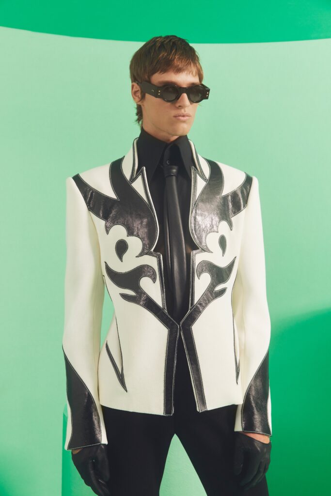 A tailored black and white blazer with intricate designs and a fitted black shirt underneath.