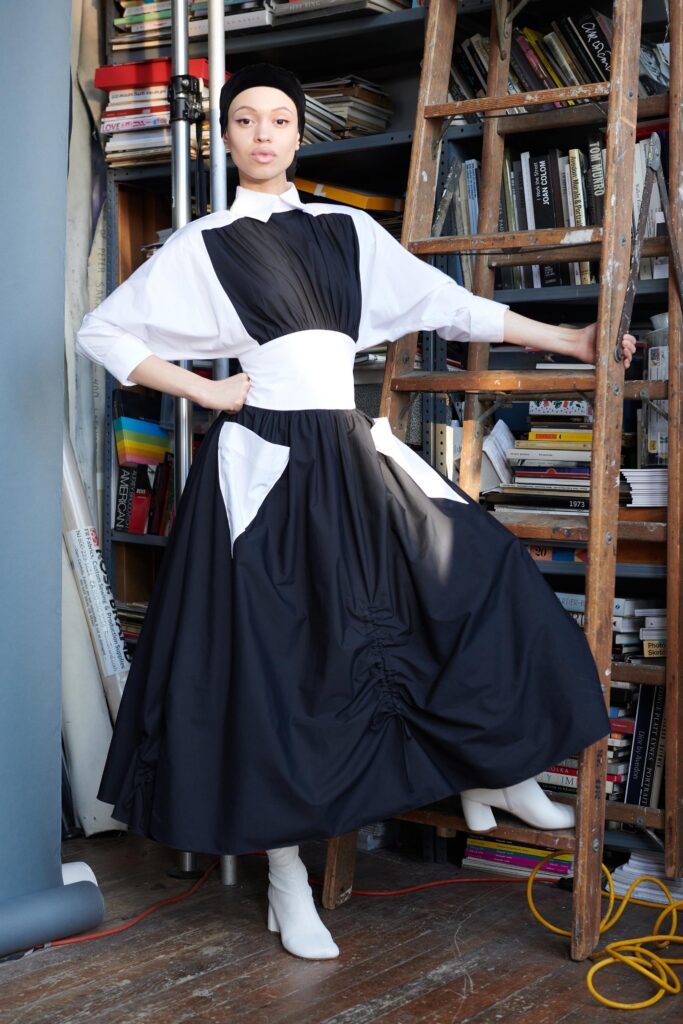 A relaxed black and white dress with long sleeves, a collared neckline, and pleated asymmetric design.