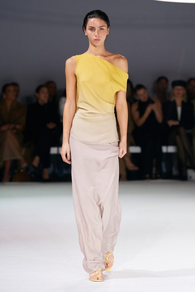 A fitted dress featuring a sleeveless design with an asymmetric silhouette in yellow and beige.