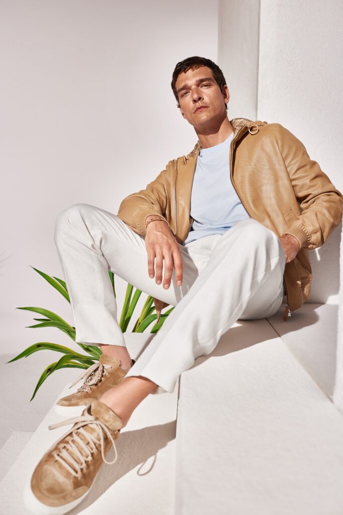 A relaxed brown leather jacket with long sleeves paired with white cotton pants.