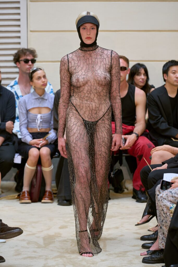 A fitted black lace dress with a high neckline and sheer design.