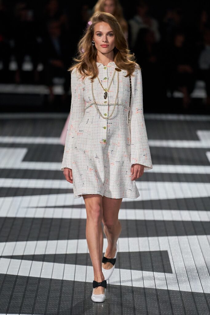 A relaxed white tweed dress with long sleeves and a collared neckline, featuring a buttoned front.