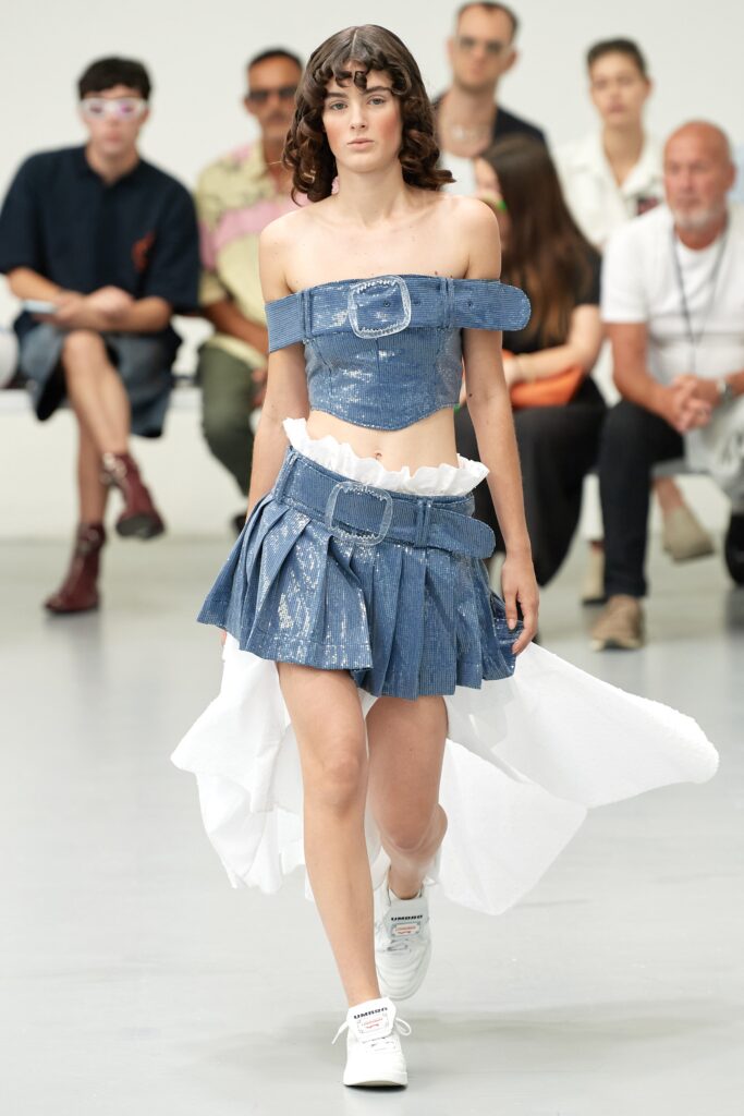 A fitted blue denim dress top with an off-shoulder design and asymmetric layered details.
