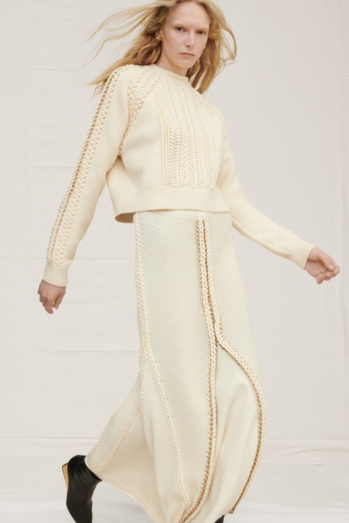 A fitted cream sweater with long sleeves paired with a matching skirt featuring a slit detail.