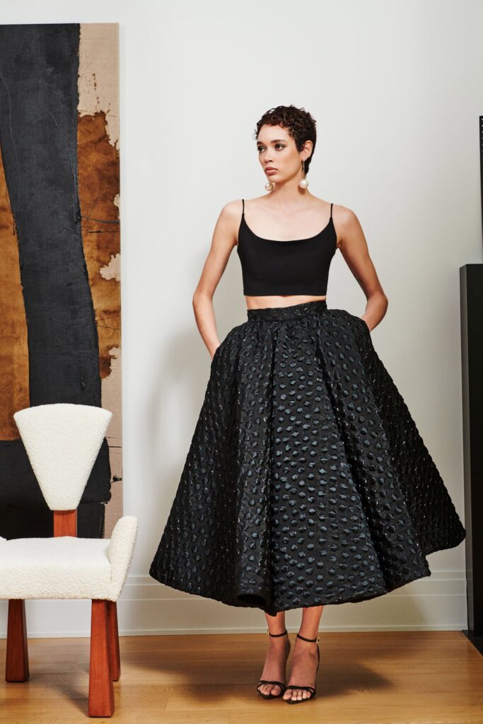 A fitted black sleeveless top paired with a high-waisted pleated A-line skirt.