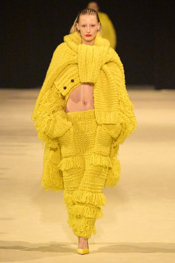 An oversized yellow knit sweater with long sleeves and fringed details paired with matching pants.