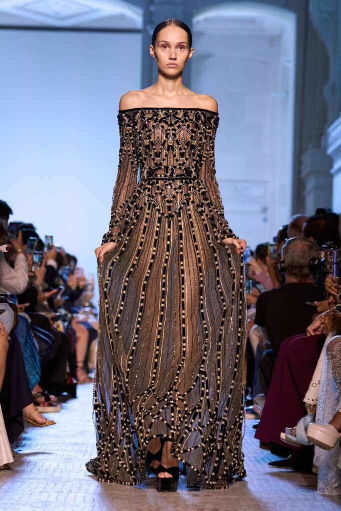 A fitted black silk off-shoulder dress with long sleeves and layered embroidered details.