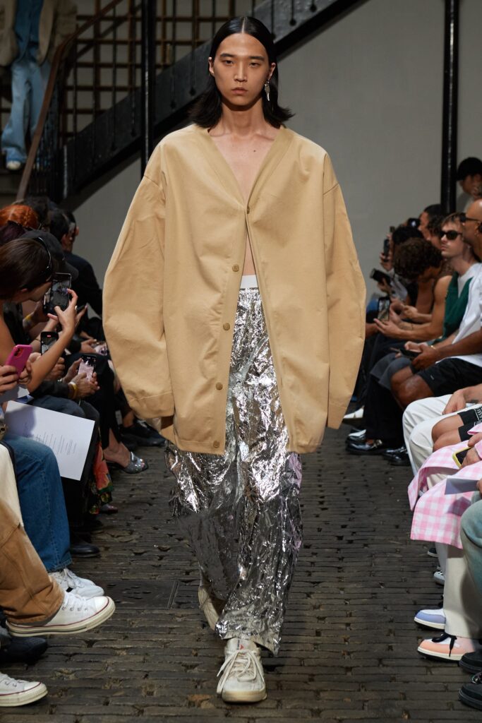 An oversized beige jacket paired with metallic silver straight-leg pants for a bold runway look.
