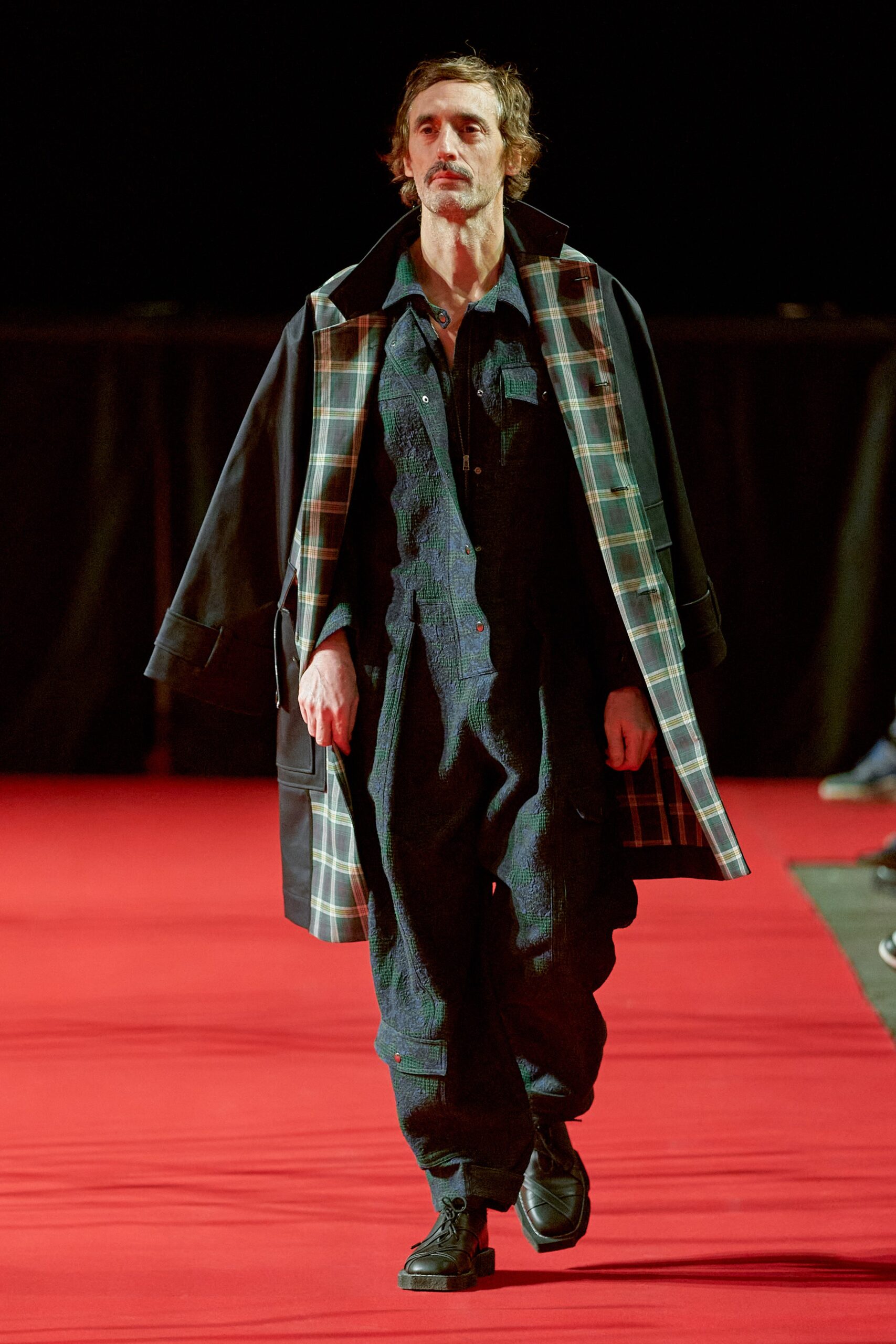 A relaxed black denim jumpsuit paired with a long-sleeve collared jacket.