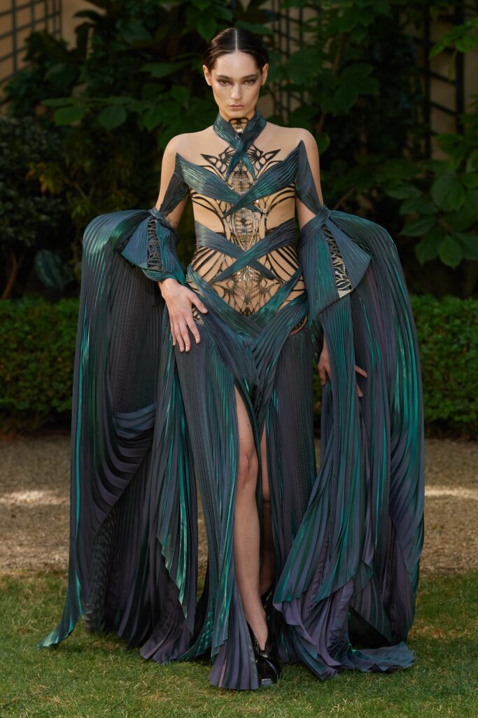 A fitted green and black sleeveless dress with a V-neckline and pleated asymmetric design.