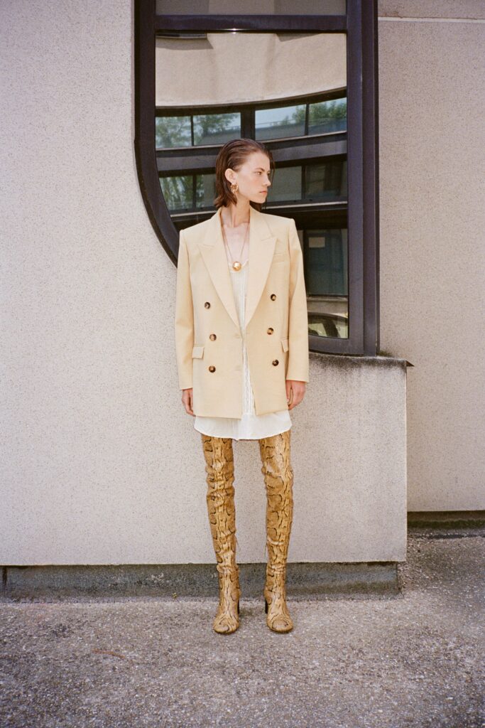A fitted beige blazer worn over a layered dress, featuring a collared design and buttoned details.