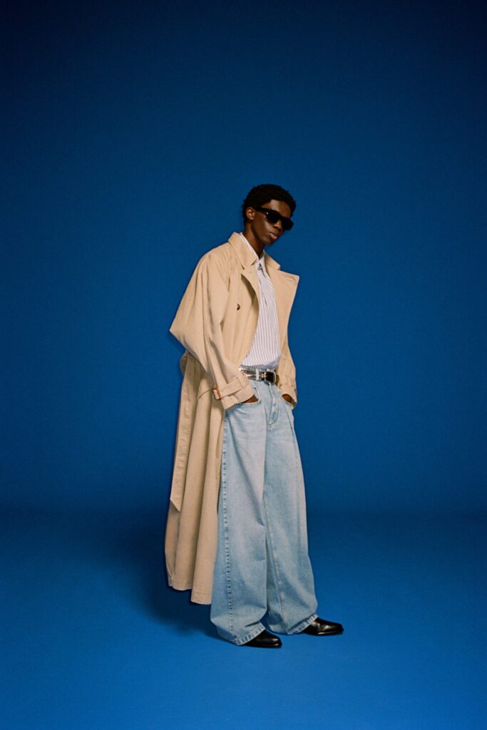 A relaxed beige coat paired with wide-leg blue denim pants and a collared shirt.