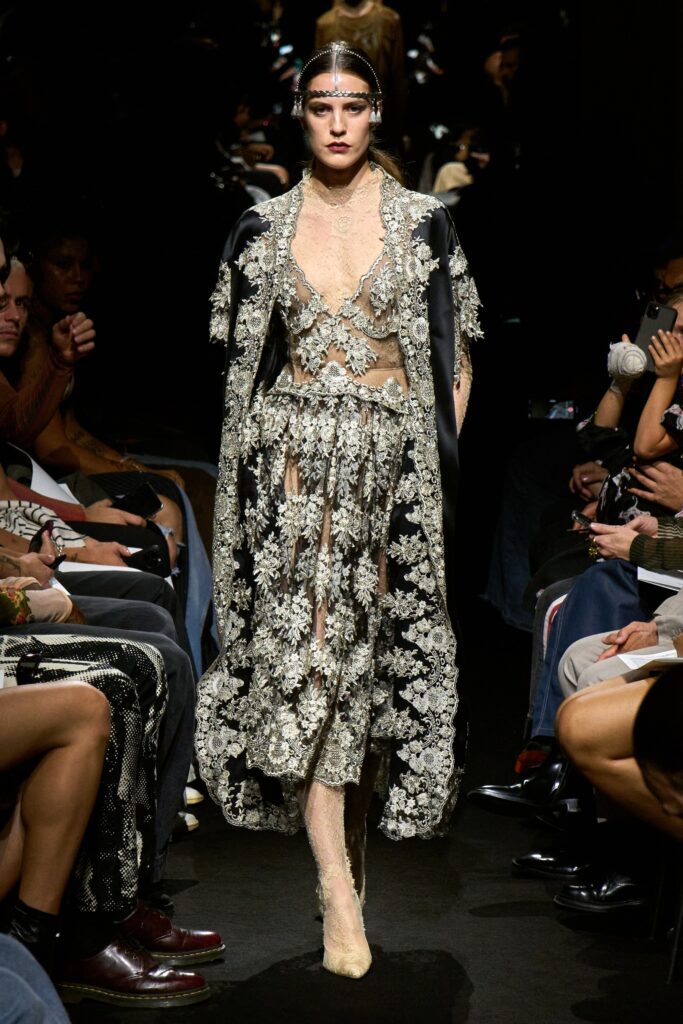 A fitted black dress with a V-neckline, layered design, and an embroidered cape.