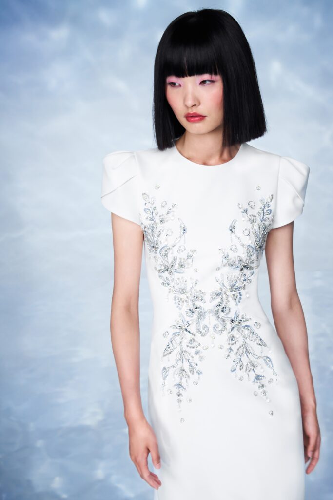 A fitted white dress with short sleeves, high neckline, and intricate embroidery.