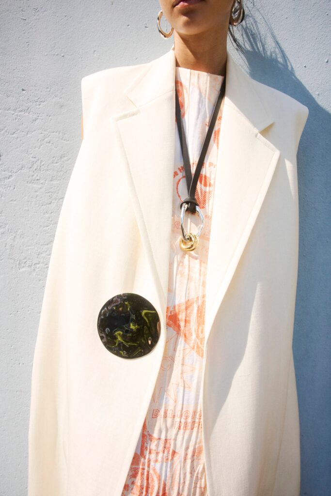 A relaxed white coat worn over a sleeveless printed dress, featuring a collared design.