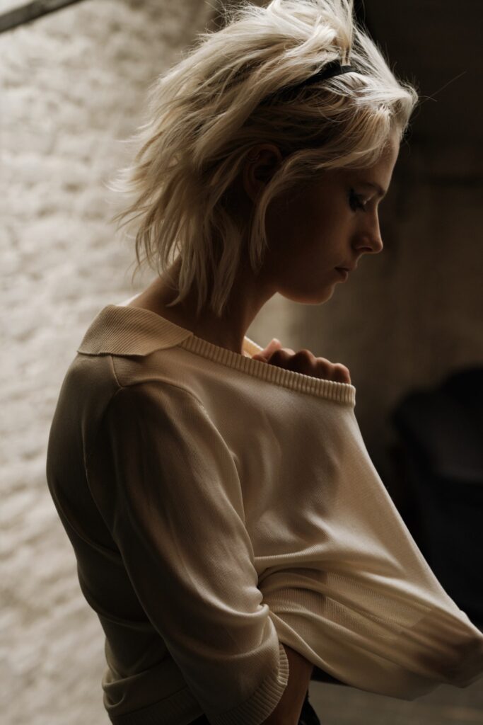 A relaxed cream cotton top with long sleeves and a collared design featuring pleated details.