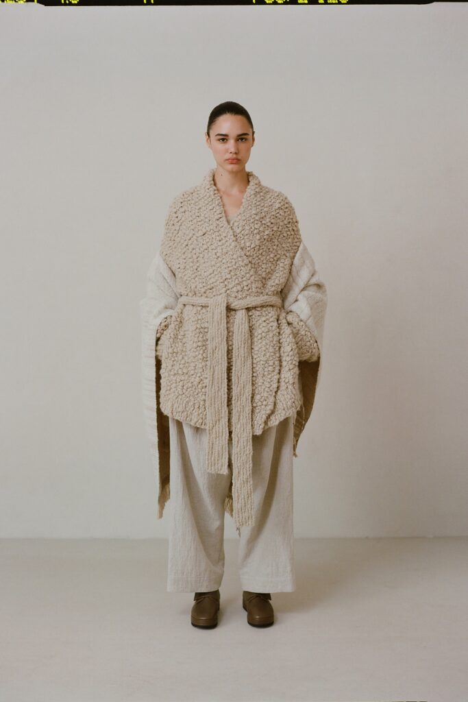 A relaxed beige wool coat with long sleeves and a belted design, paired with linen pants.