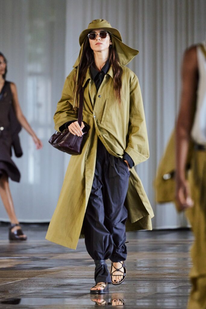 A relaxed olive coat paired with black pants, featuring a collared design and buttoned details.