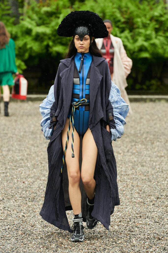 A fitted blue jumpsuit layered with a black coat featuring asymmetric design details.