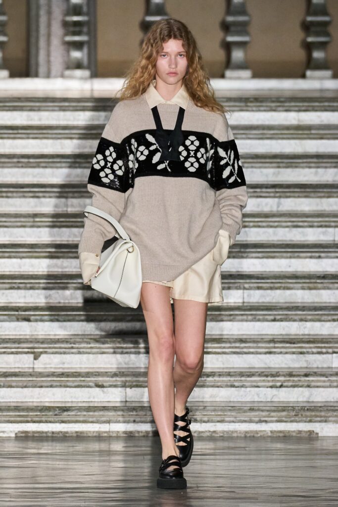 A relaxed beige and black striped sweater paired with casual shorts.