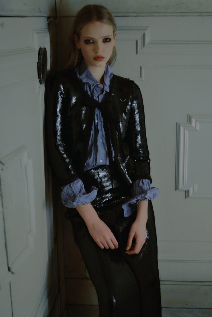 A fitted black sequin jacket paired with a blue collared shirt and a sleek skirt.