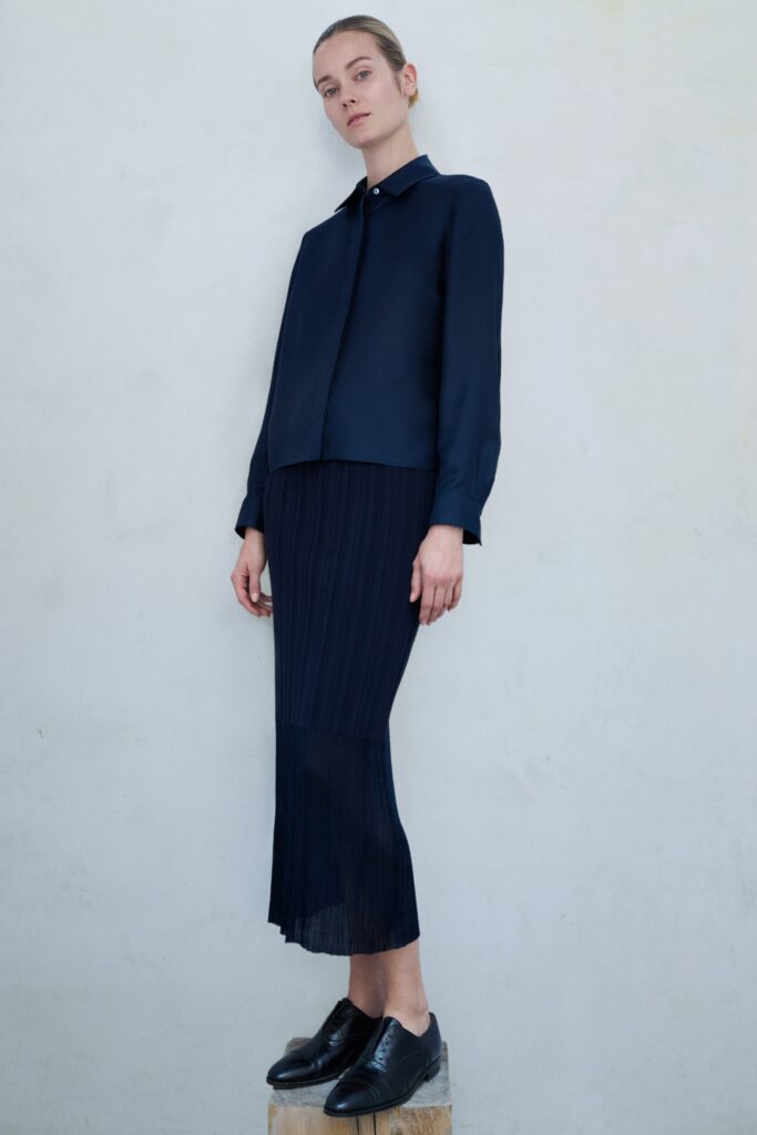 A fitted navy silk blouse with long sleeves paired with a pleated asymmetric skirt.
