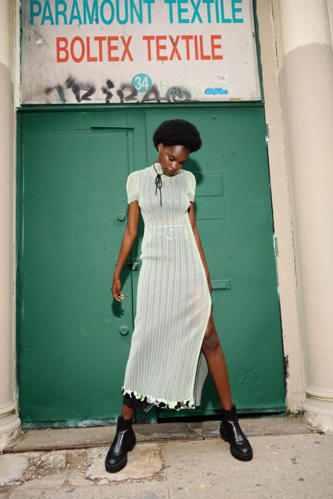 A fitted green cotton dress with short sleeves, a high neckline, and a tiered silhouette featuring a slit.