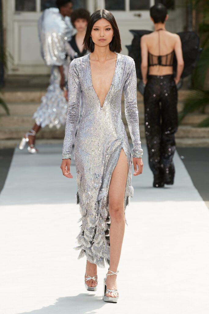 A fitted silver sequined dress with a deep V-neckline and a thigh-high slit.