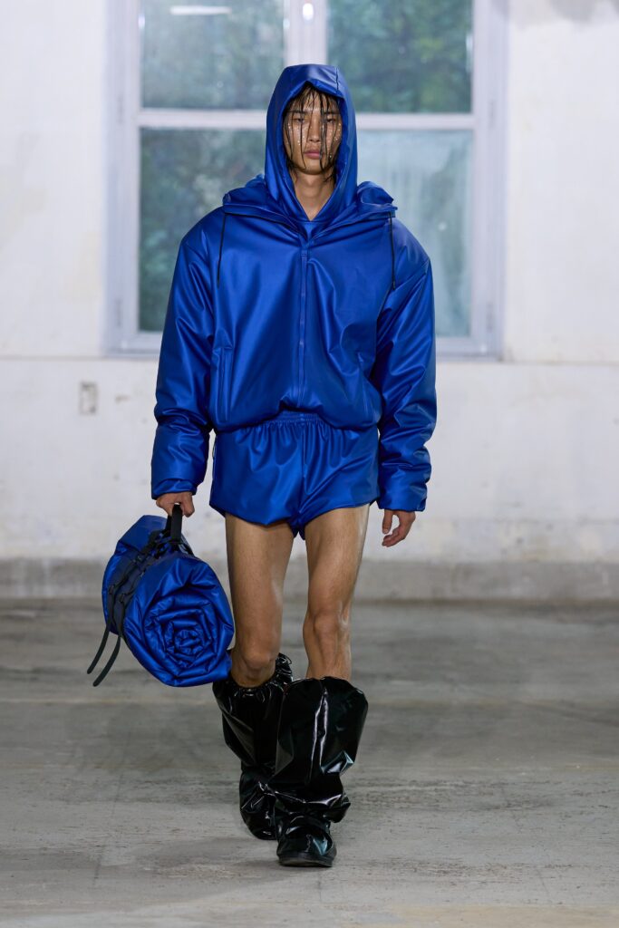 An oversized blue silk hoodie with long sleeves paired with matching shorts, featuring an asymmetric design.