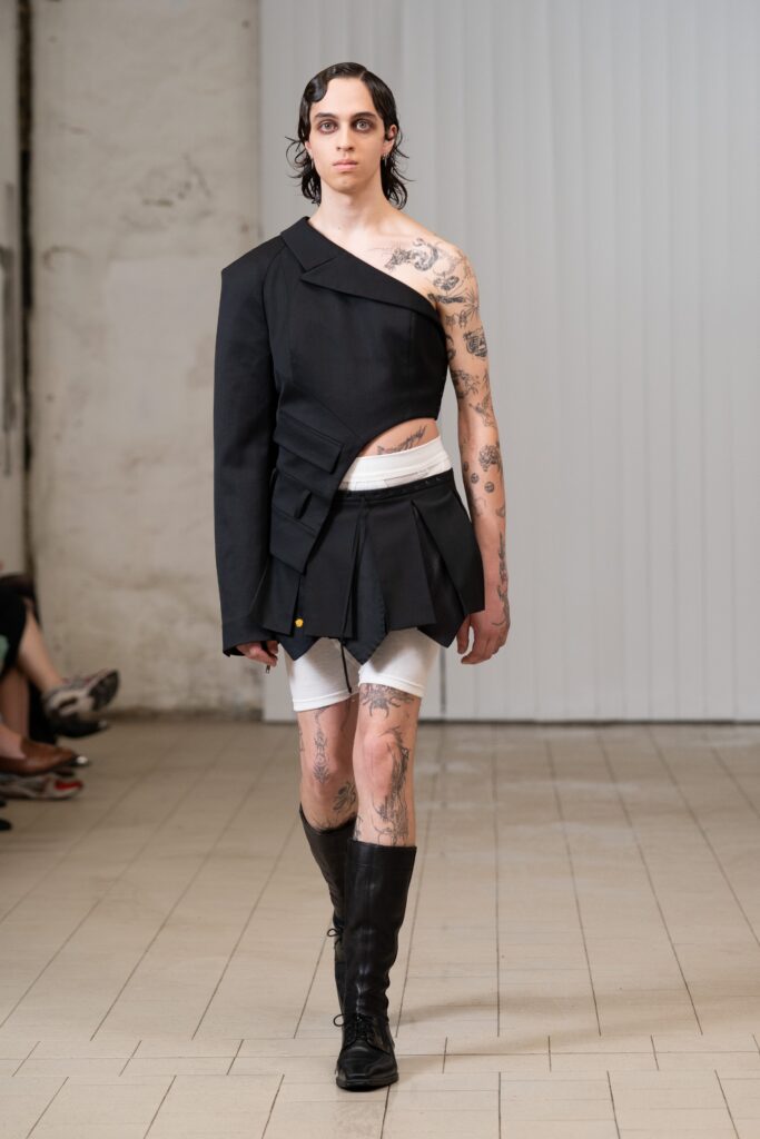 An asymmetric black fitted dress paired with a structured jacket, showcasing a unique silhouette.