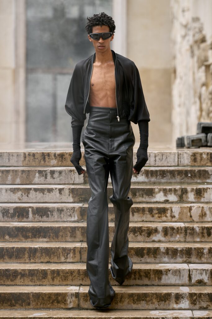 A fitted black leather jacket with long sleeves paired with flared black leather pants.