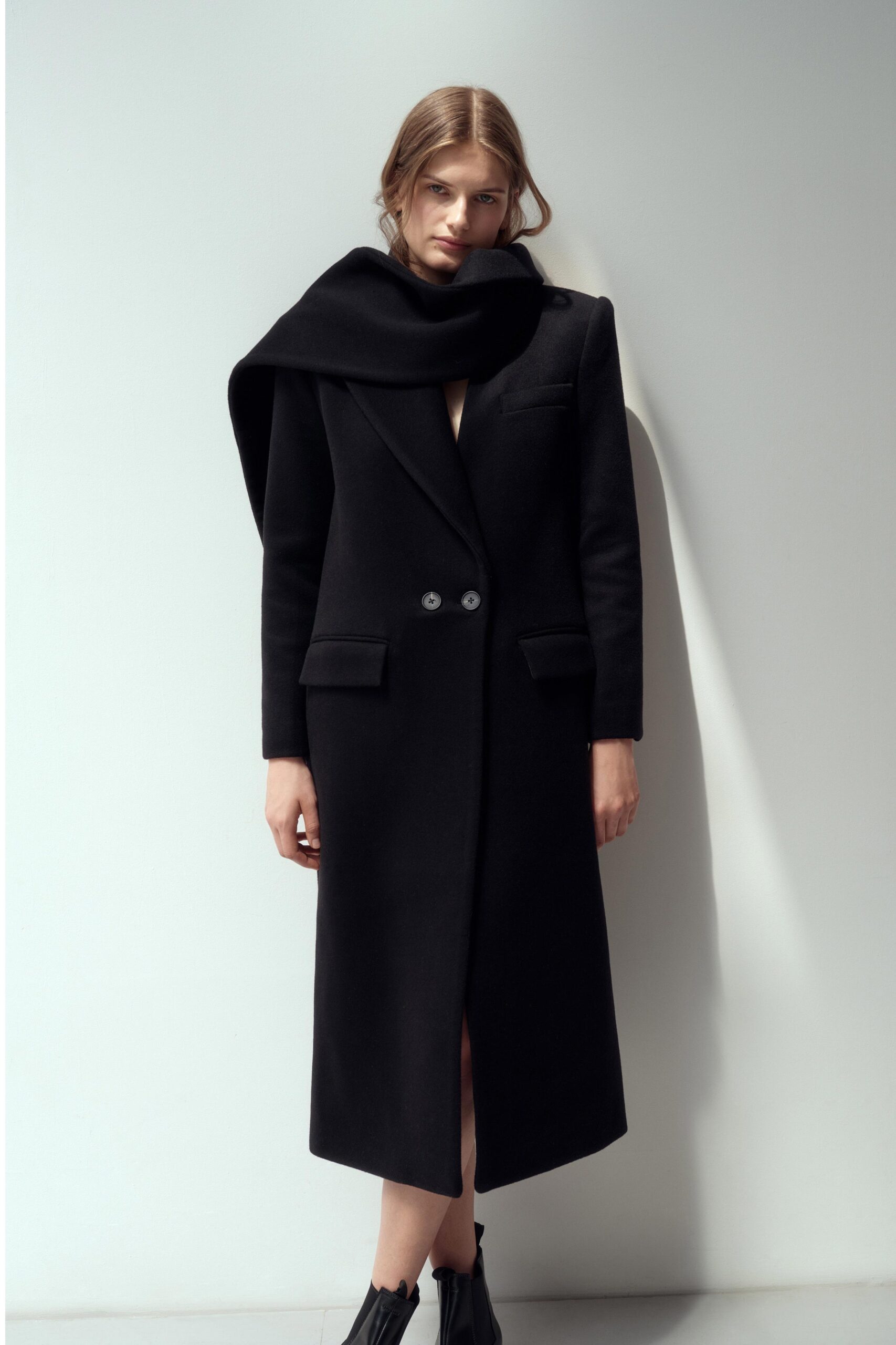 A fitted black wool coat with long sleeves and a collared design, featuring button details.