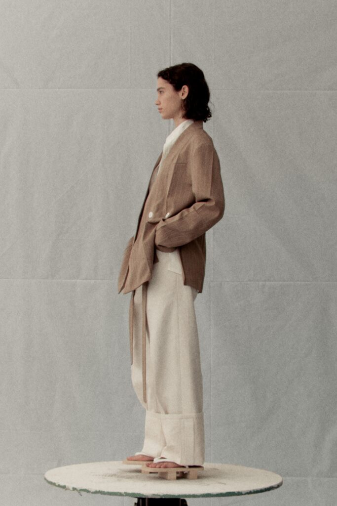 A relaxed beige cotton jacket with long sleeves and collared design paired with wide-leg pants.