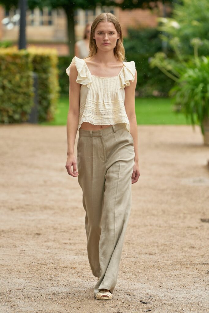 A relaxed beige sleeveless top with ruffles paired with loose-fitting linen pants.