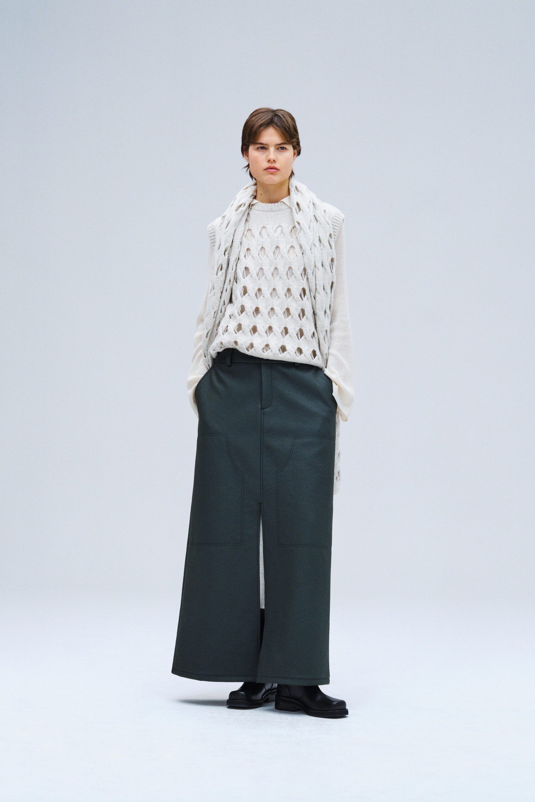 A relaxed white wool sleeveless sweater paired with a pleated gray skirt featuring an asymmetric design.