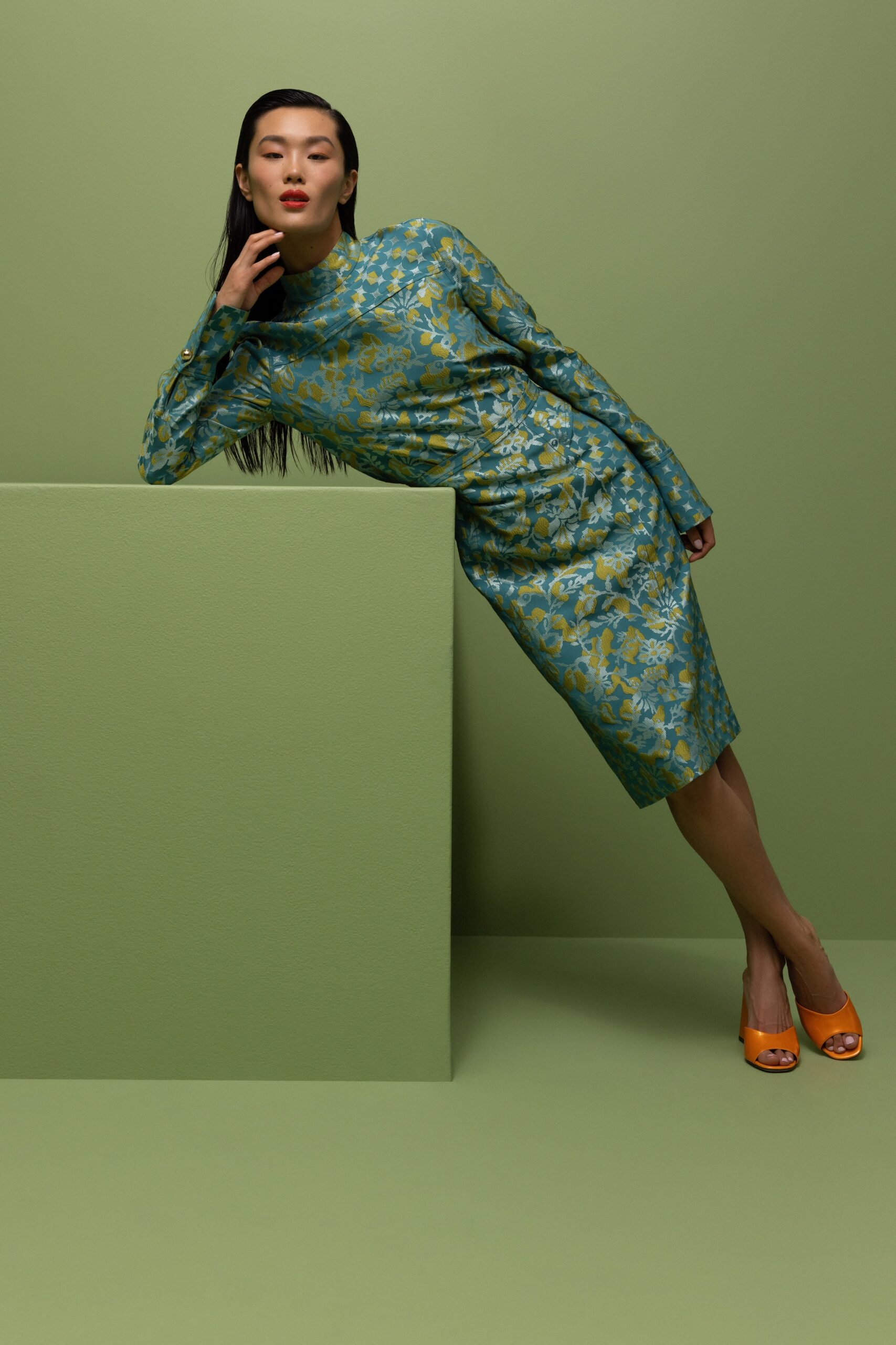 A fitted green silk dress with long sleeves and a high neckline featuring a floral pattern.