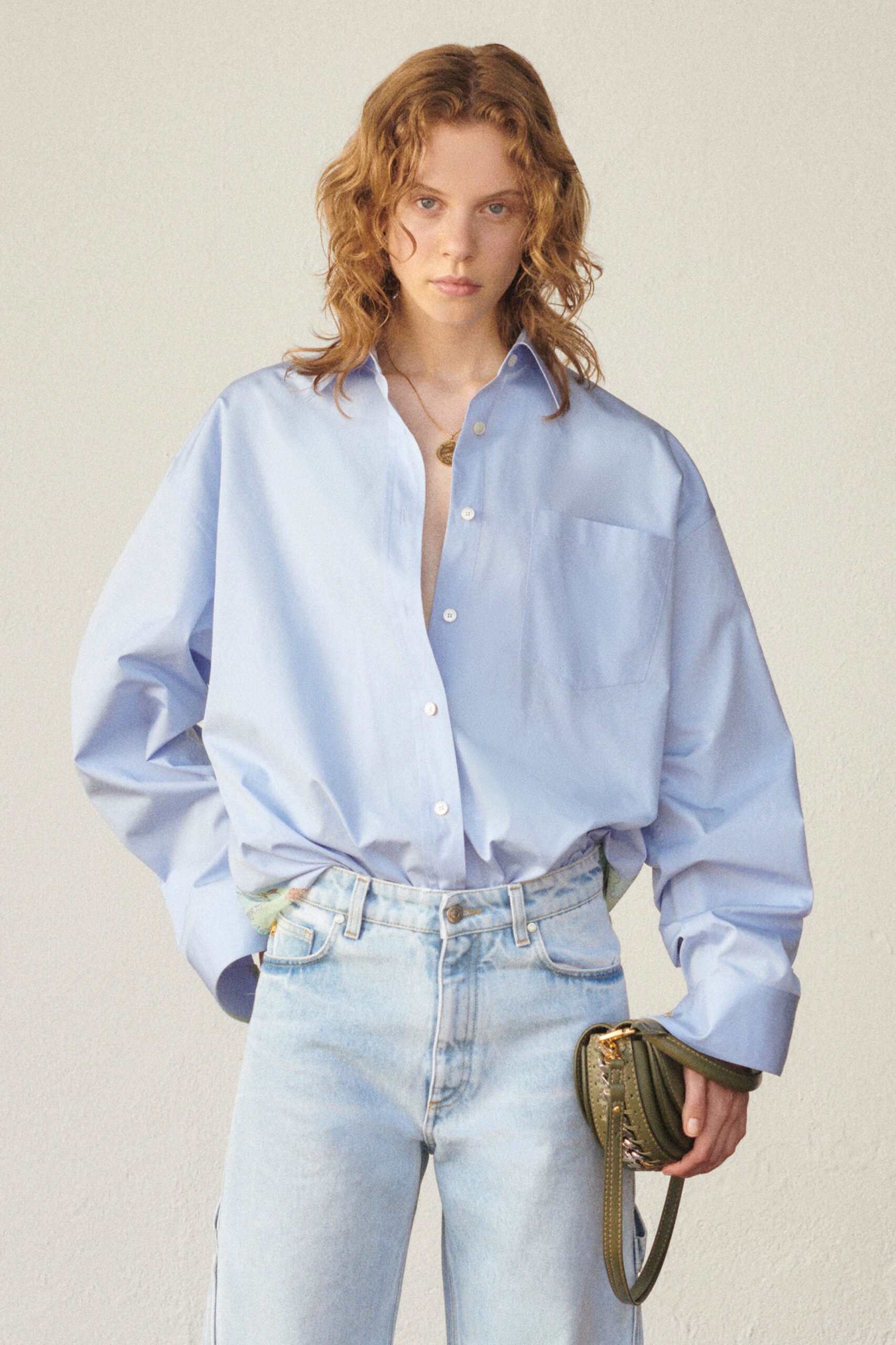 A relaxed blue cotton shirt with long sleeves and a collared neckline paired with straight-leg jeans.