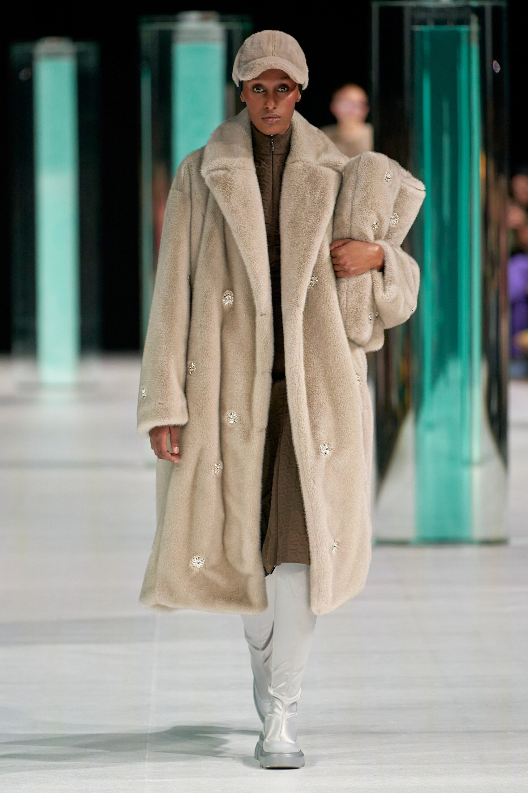 A relaxed beige fur coat worn over a high-neck dress with long sleeves.