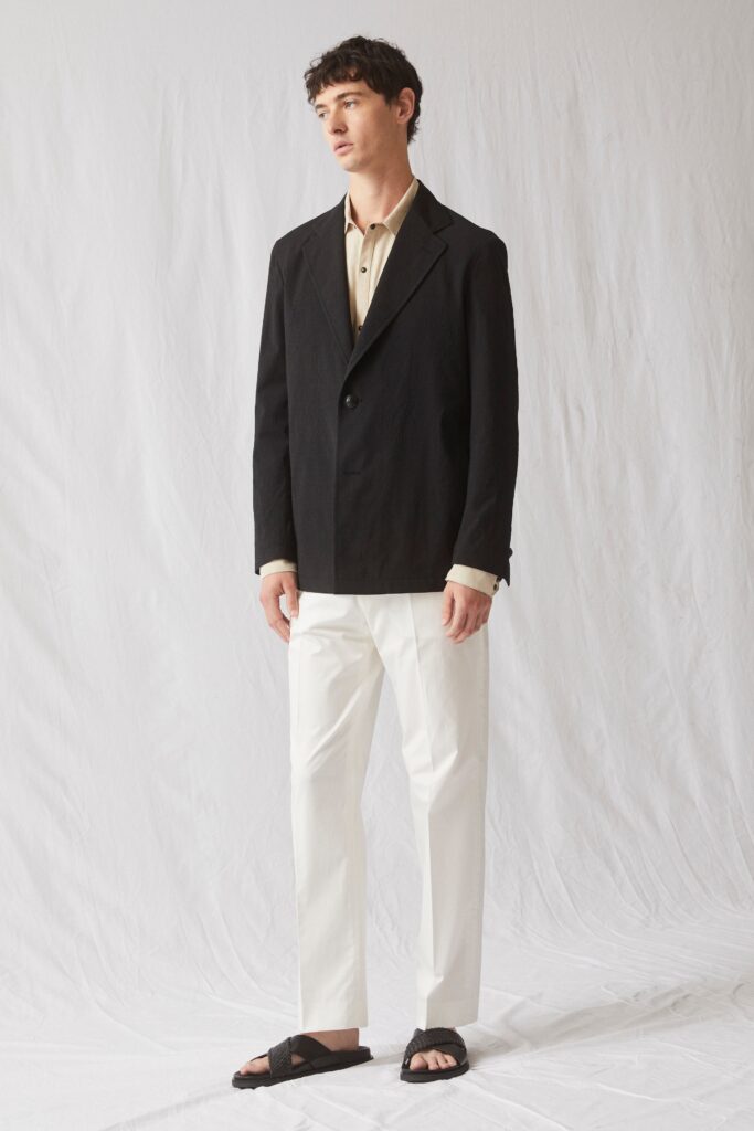 A relaxed black jacket with long sleeves and a collared shirt paired with white pants.
