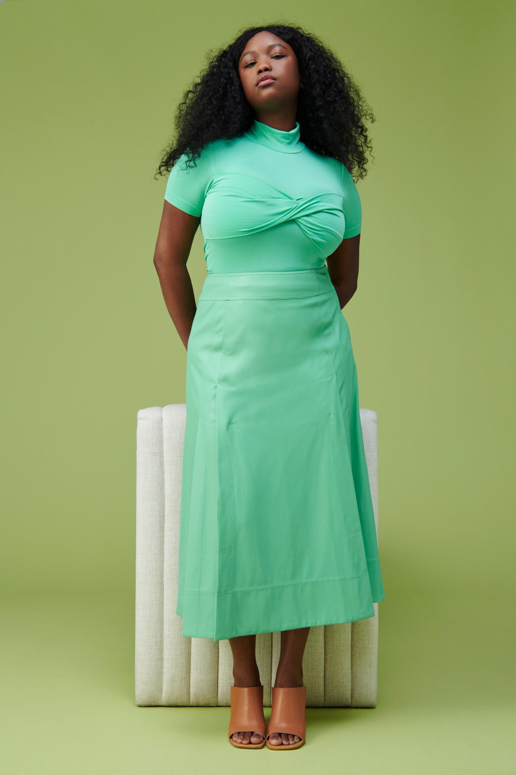 A fitted green top with short sleeves and a high-neck paired with a straight-leg skirt.